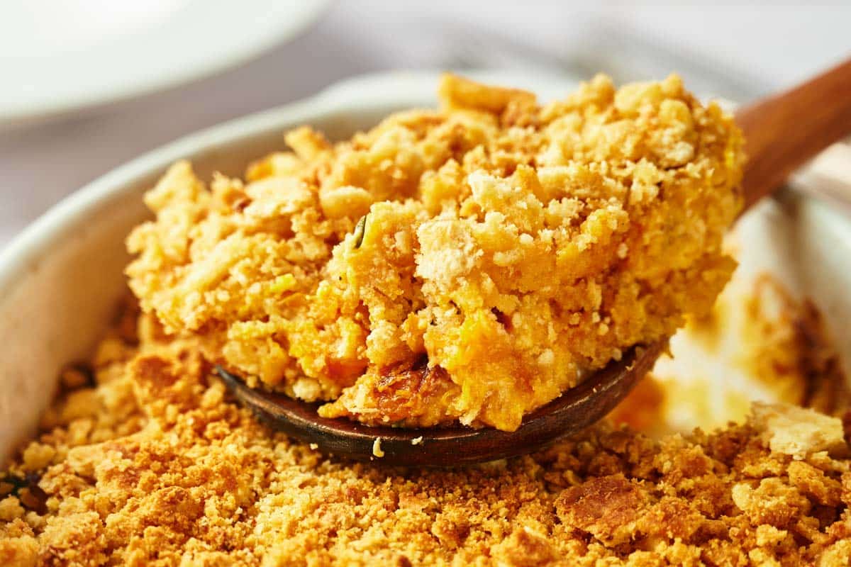 A close-up of a serving of fruit crumble being scooped out of a baking dish with a wooden spoon.