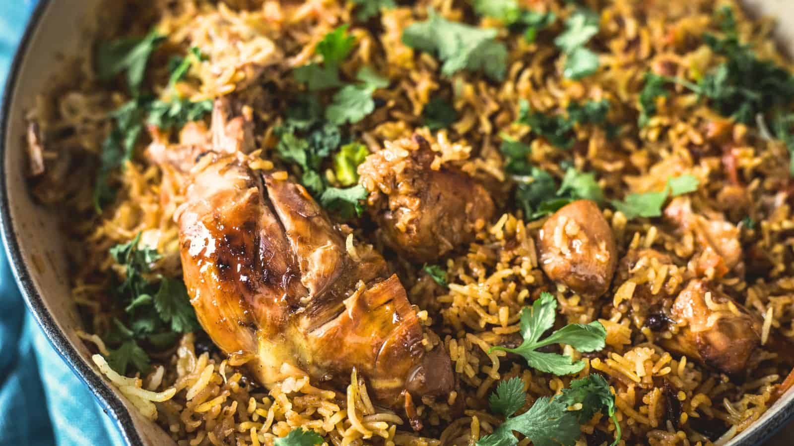 Close-up of a pan filled with chicken biryani, showing pieces of cooked chicken, spiced rice, and garnished with fresh cilantro.