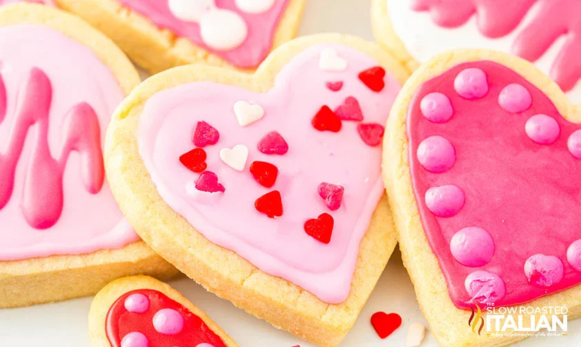 Heart-shaped sugar cookies decorated with pink and white icing, topped with small heart-shaped and round sprinkles.
