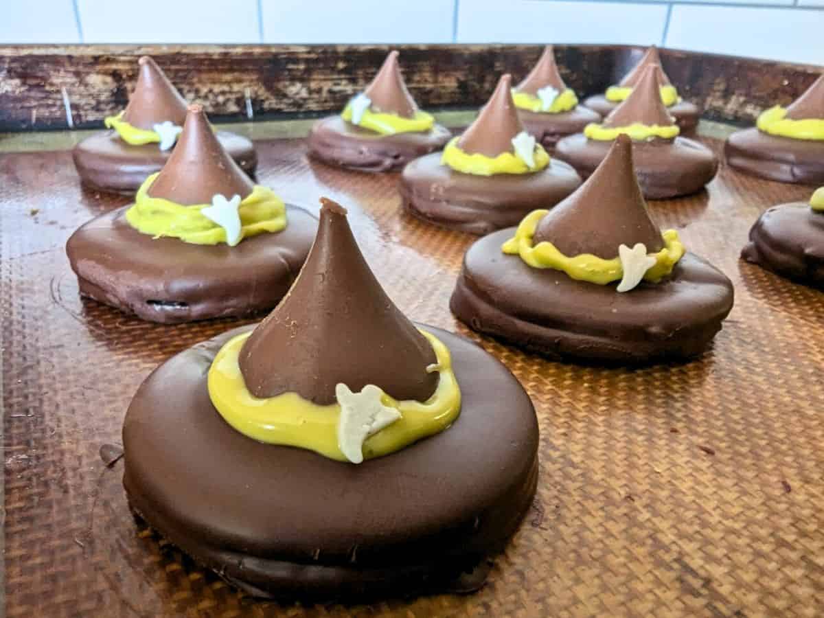 Chocolate cookies topped with candy kisses, yellow icing rings, and small white bone decorations, arranged on a baking tray.
