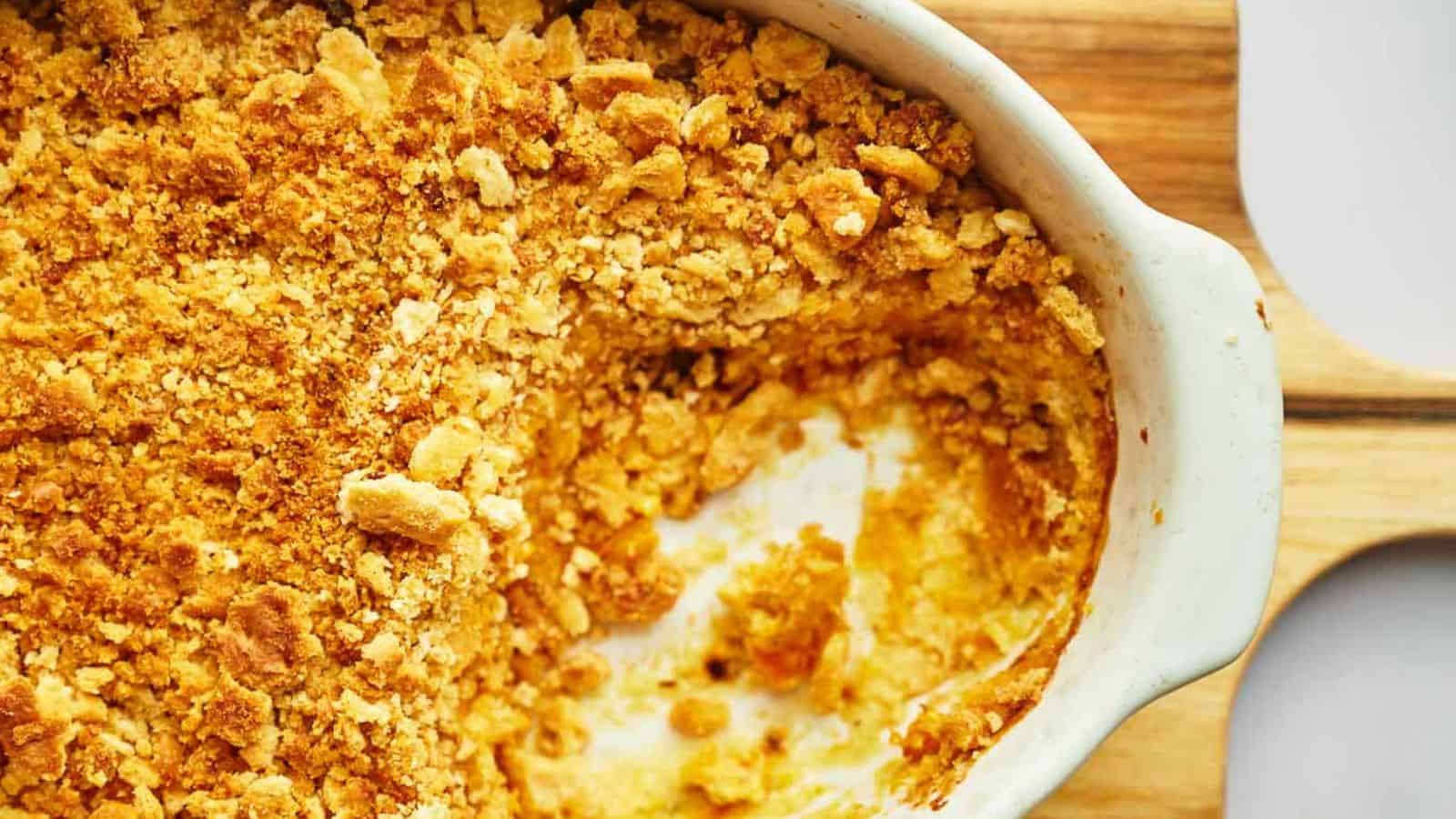 A partially eaten baked casserole with a golden, crumbly topping in a white dish on a wooden surface.