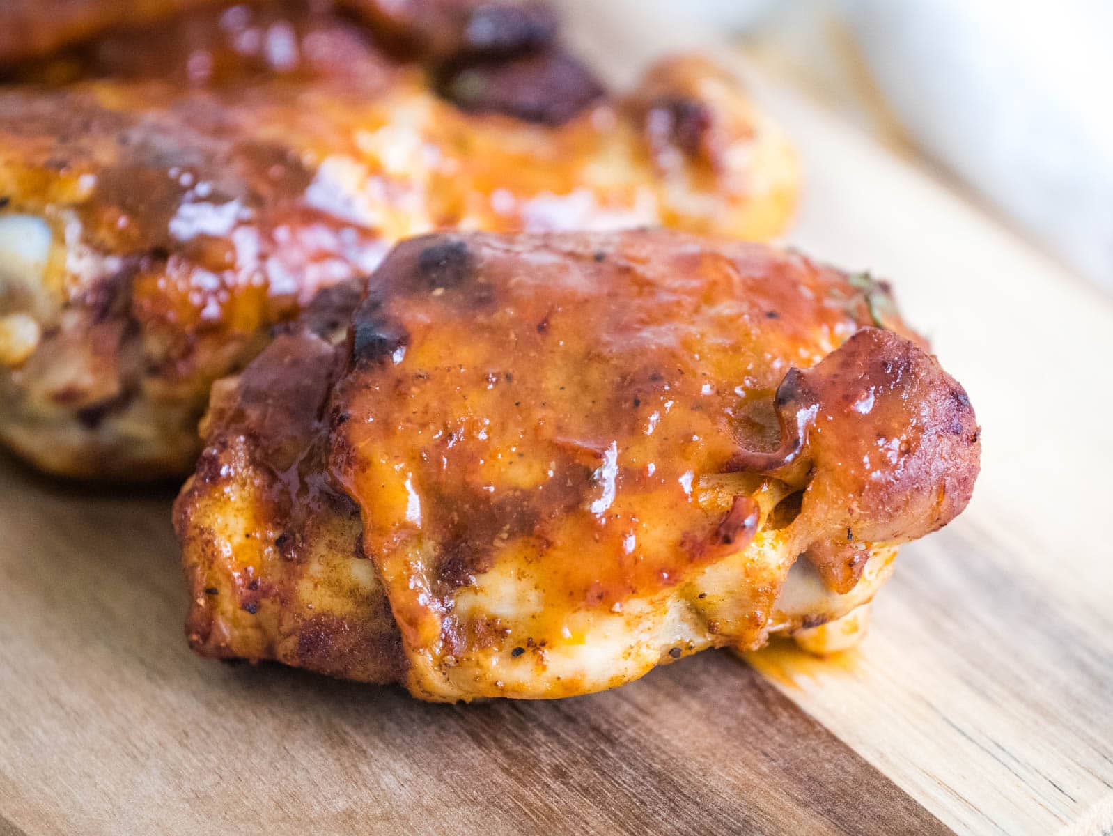 Close-up of a piece of glazed barbecue chicken on a wooden cutting board.