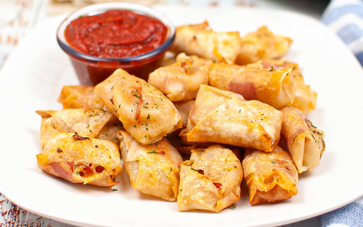 A plate of golden-brown baked pizza rolls is served with a small bowl of red marinara dipping sauce.
