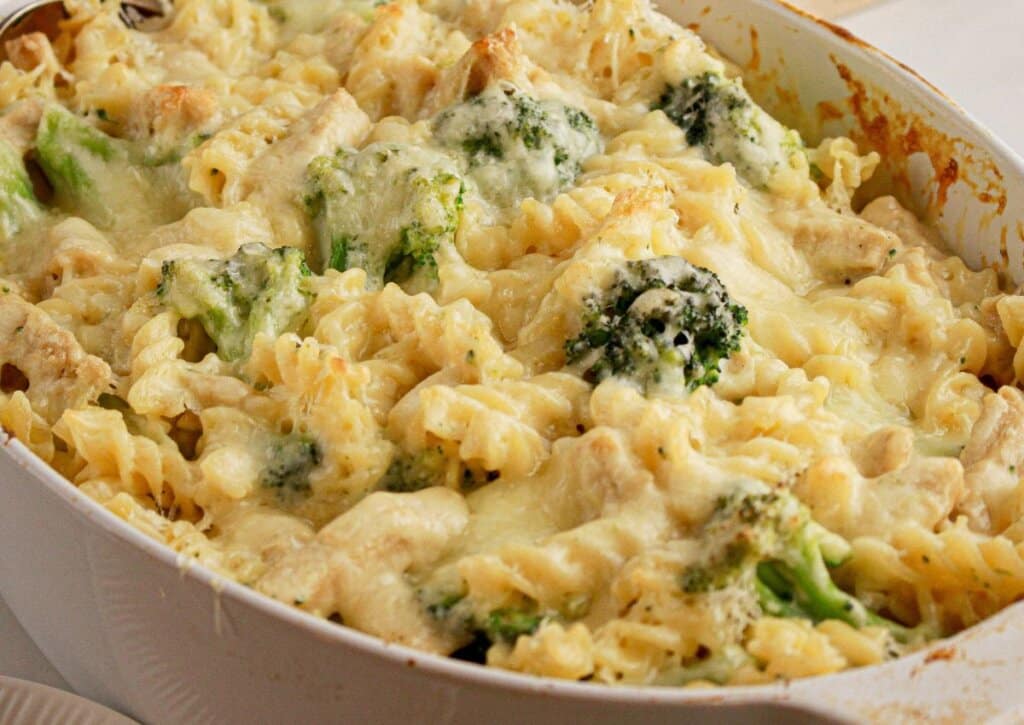 A baked casserole dish filled with rotini pasta, pieces of chicken, broccoli florets, and melted cheese on top.