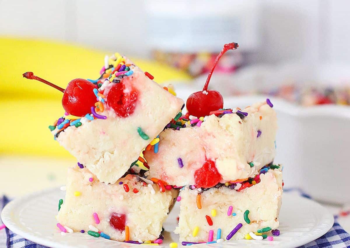 Three pieces of white fudge with colorful sprinkles and cherries stacked on a plate.
