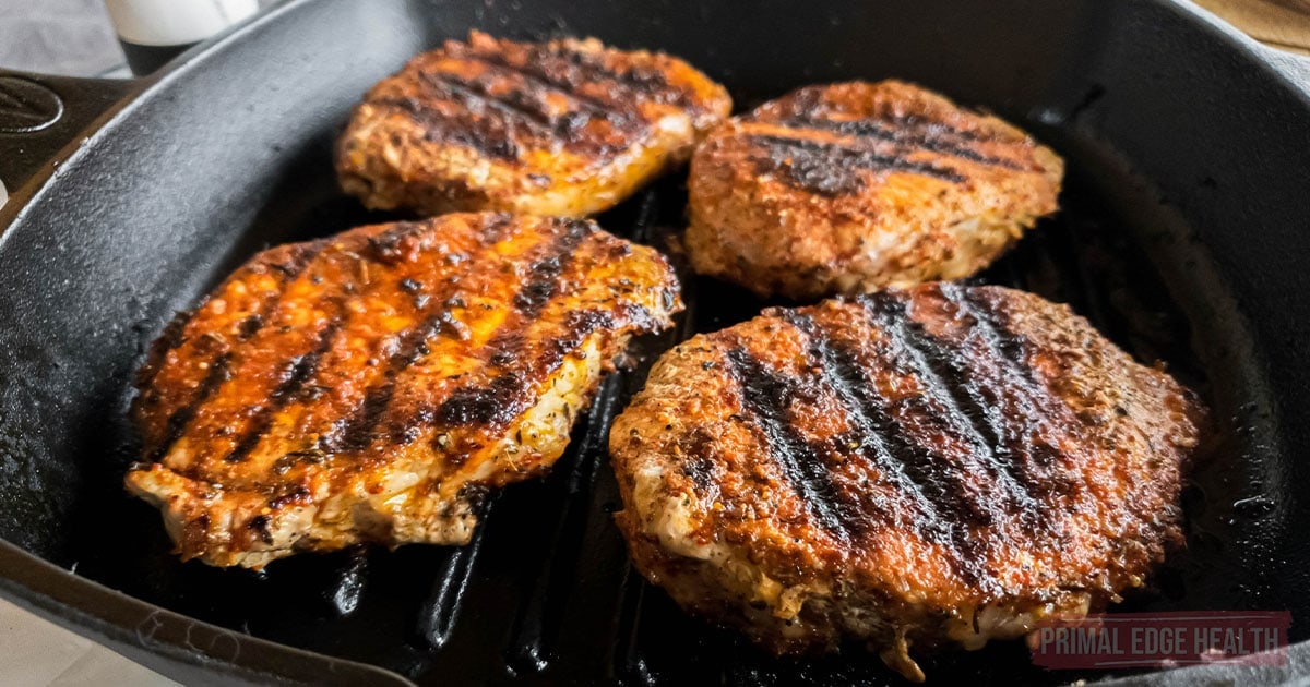 Four grilled burger patties with char marks cooking in a black cast iron grill pan.
