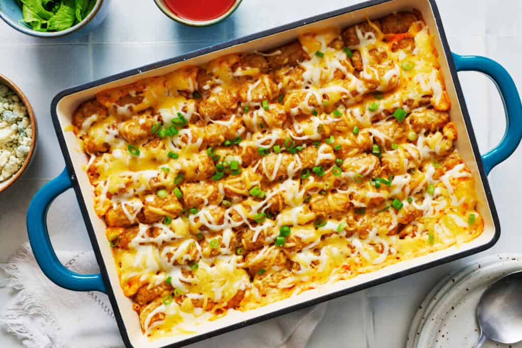 A rectangular casserole dish filled with tater tot hotdish, topped with melted cheese and chopped green onions.