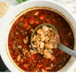 A pot of stew with diced vegetables and meat, with a ladle lifting a portion from the pot.