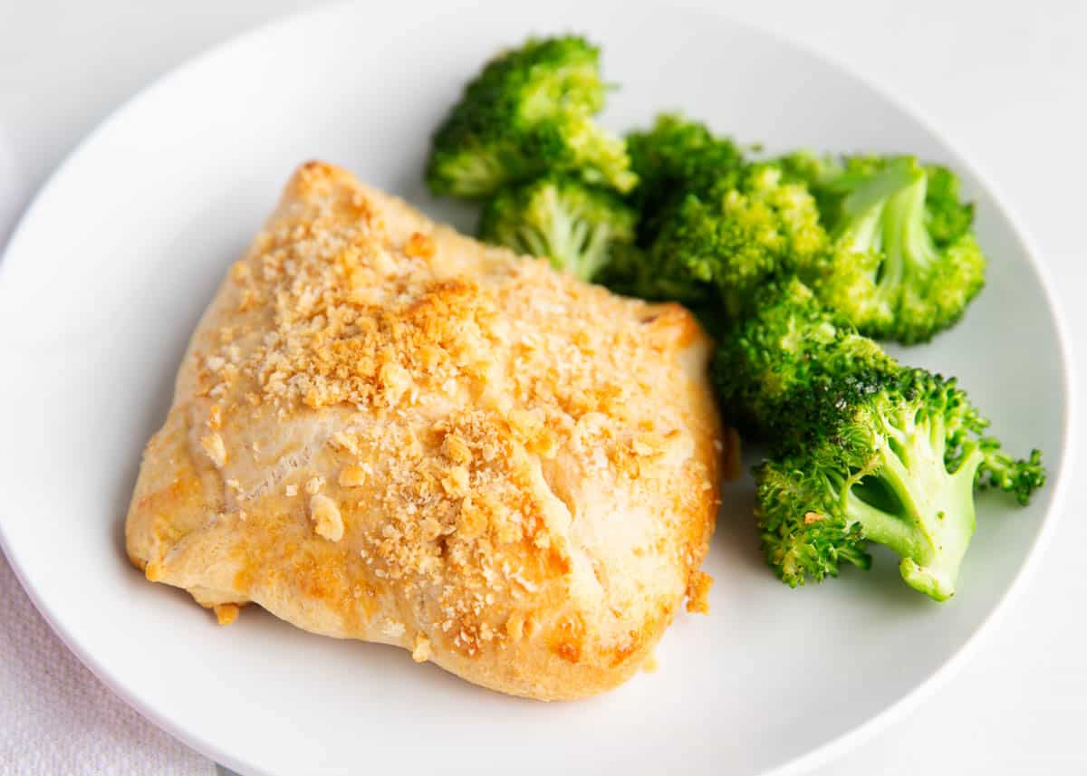 A white plate with a baked, golden-brown pastry topped with crumbs and a serving of steamed broccoli.