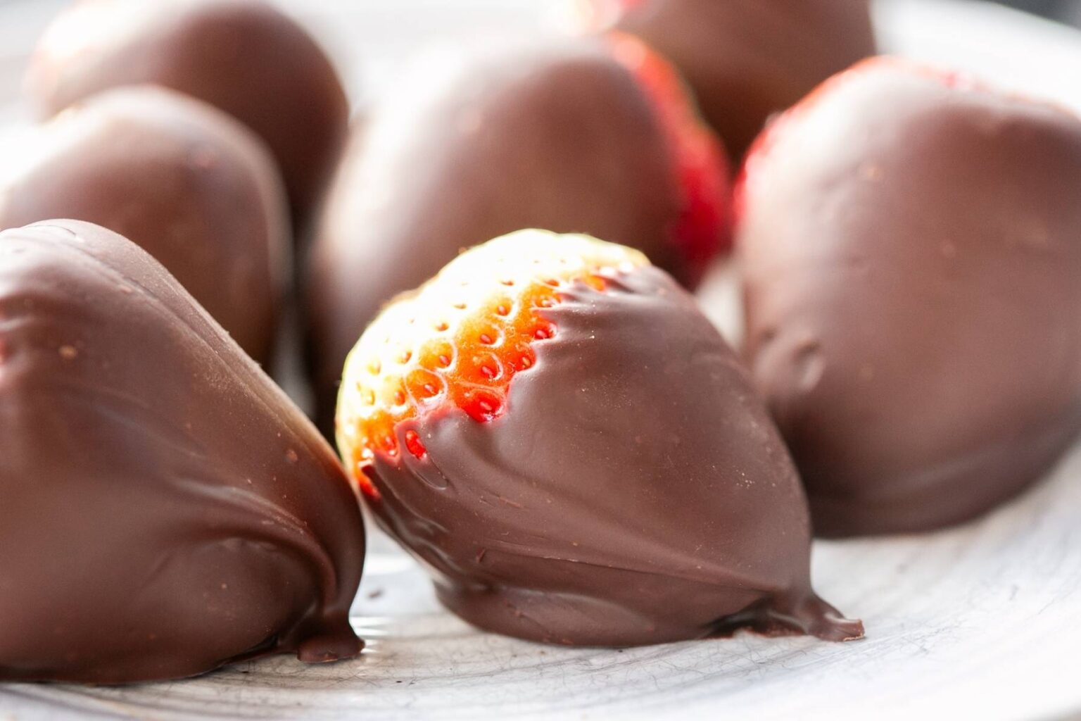 Close-up of several strawberries partially coated in chocolate, arranged on a light-colored plate.