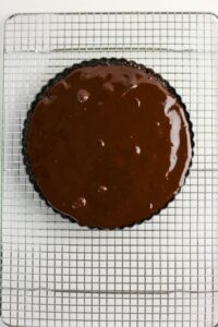 A round baking tin filled with chocolate batter sits on a metal cooling rack atop a white surface.