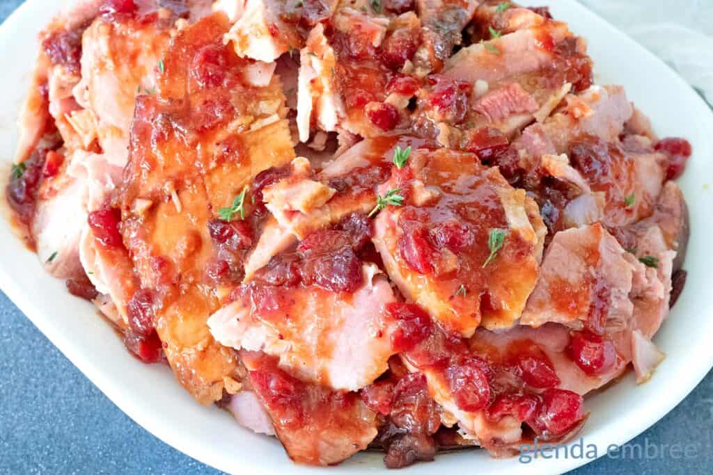 Sliced ham topped with a chunky cranberry glaze, served on a white plate.