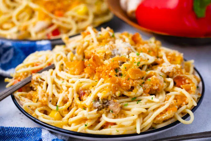 A close-up of a plate of baked spaghetti topped with a crispy breadcrumb and cheese mixture, with a fork placed on the side.