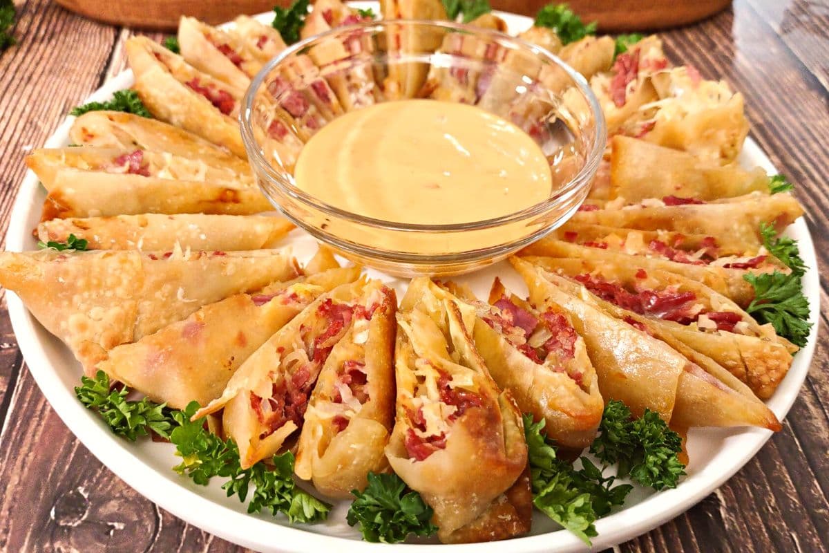 A plate of sliced stuffed egg rolls arranged in a circle around a bowl of dipping sauce, garnished with fresh parsley.