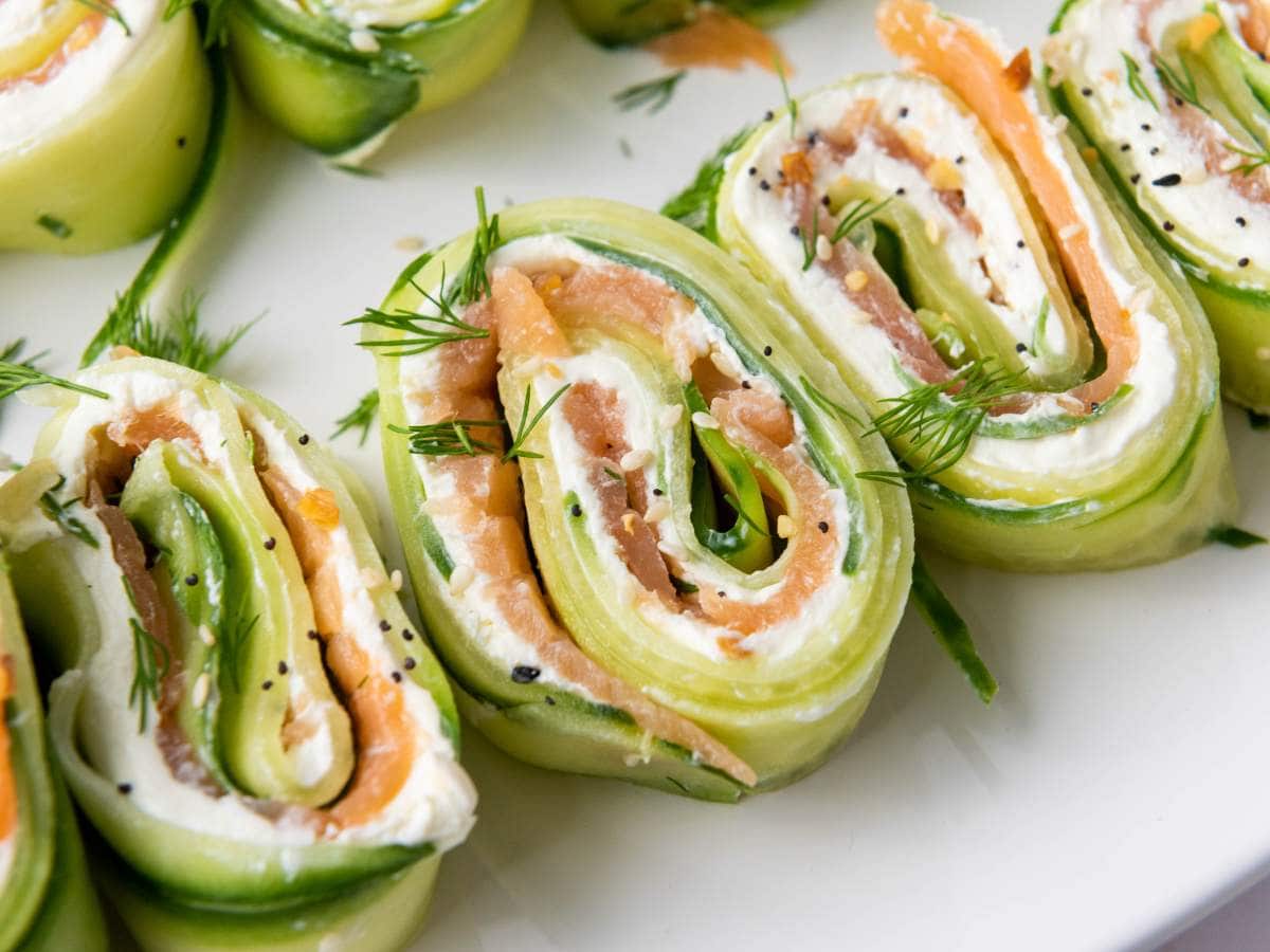 Close-up of cucumber roll-ups filled with cream cheese, smoked salmon, and fresh dill, arranged on a white plate.