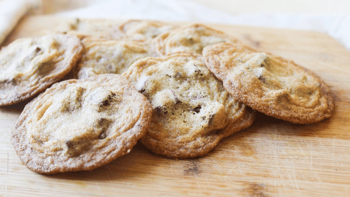 A group of chocolate chip cookies is arranged on a wooden cutting board.