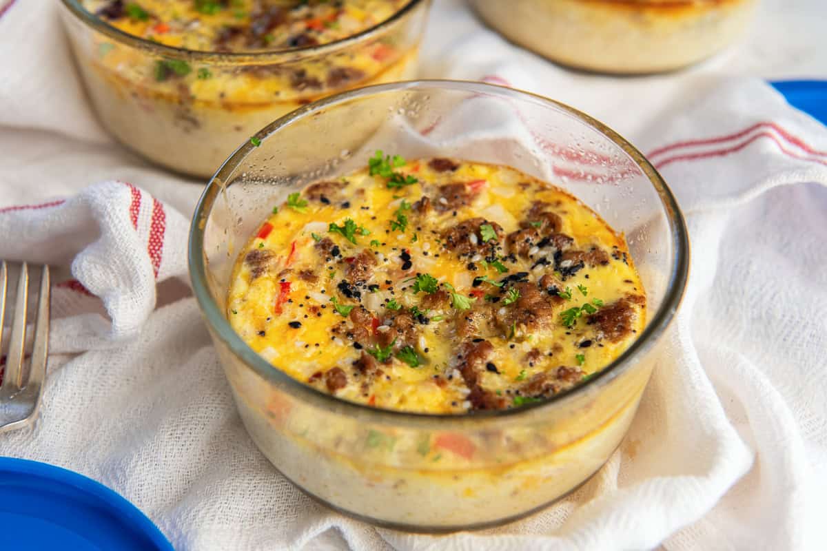 A glass bowl filled with a baked egg dish containing sausage, cheese, and herbs, placed on a white cloth.