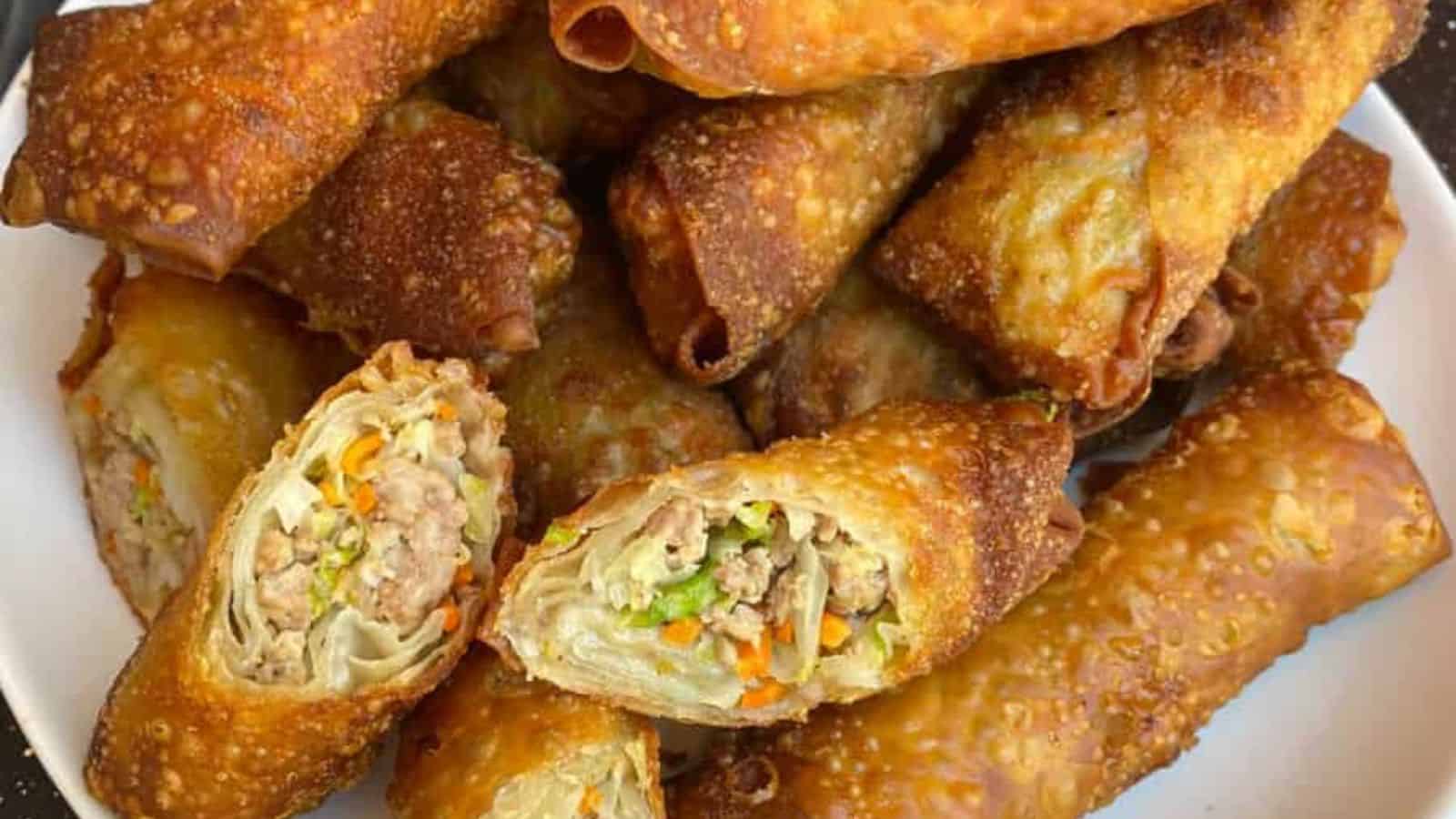 A plate of crispy fried egg rolls, some whole and some cut open to show a filling of ground meat and mixed vegetables.