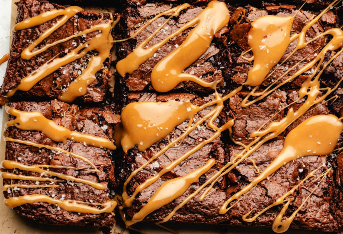 Close-up of chocolate brownies cut into squares, topped with drizzled caramel sauce and sprinkled with coarse salt.