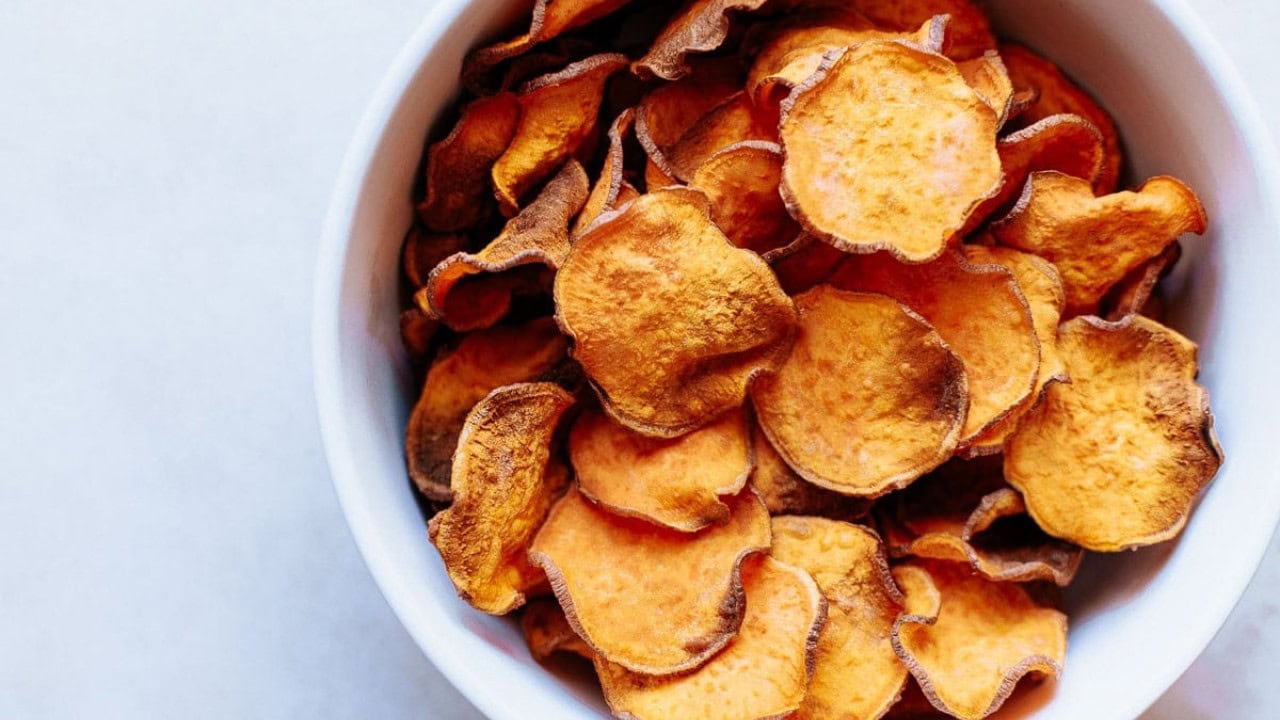 A white bowl filled with crispy, thinly sliced sweet potato chips viewed from above.