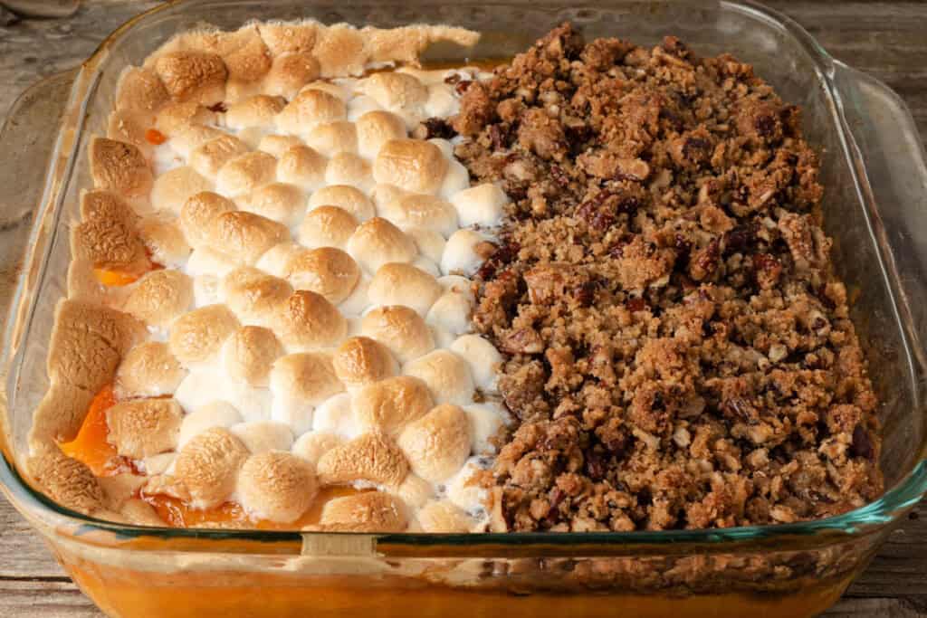 Glass baking dish with a sweet potato casserole, half topped with toasted marshmallows and half with a pecan streusel crumb topping.