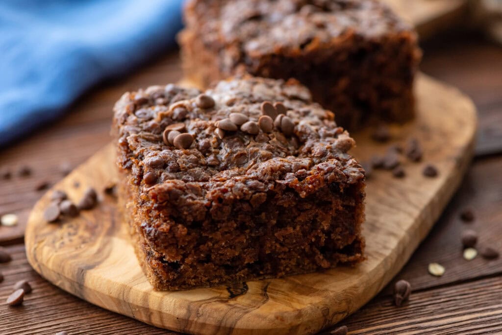 Two pieces of chocolate chip banana bread sit on a wooden board, topped with chocolate chips and surrounded by a few scattered chips.