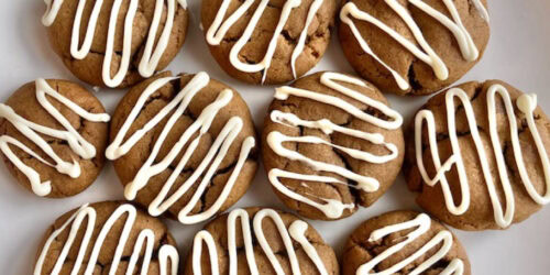 A batch of round cookies with white icing drizzled in zigzag patterns arranged on a white surface.