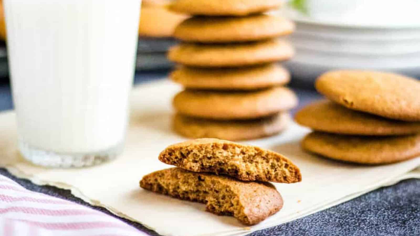 A glass of milk next to a stack of cookies, with one cookie broken in half on a white surface.