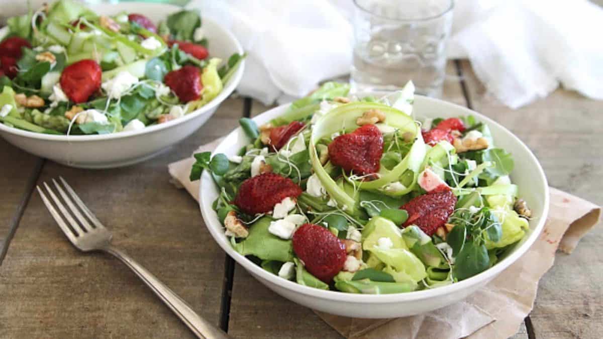 Two bowls of salad with strawberries and nuts.