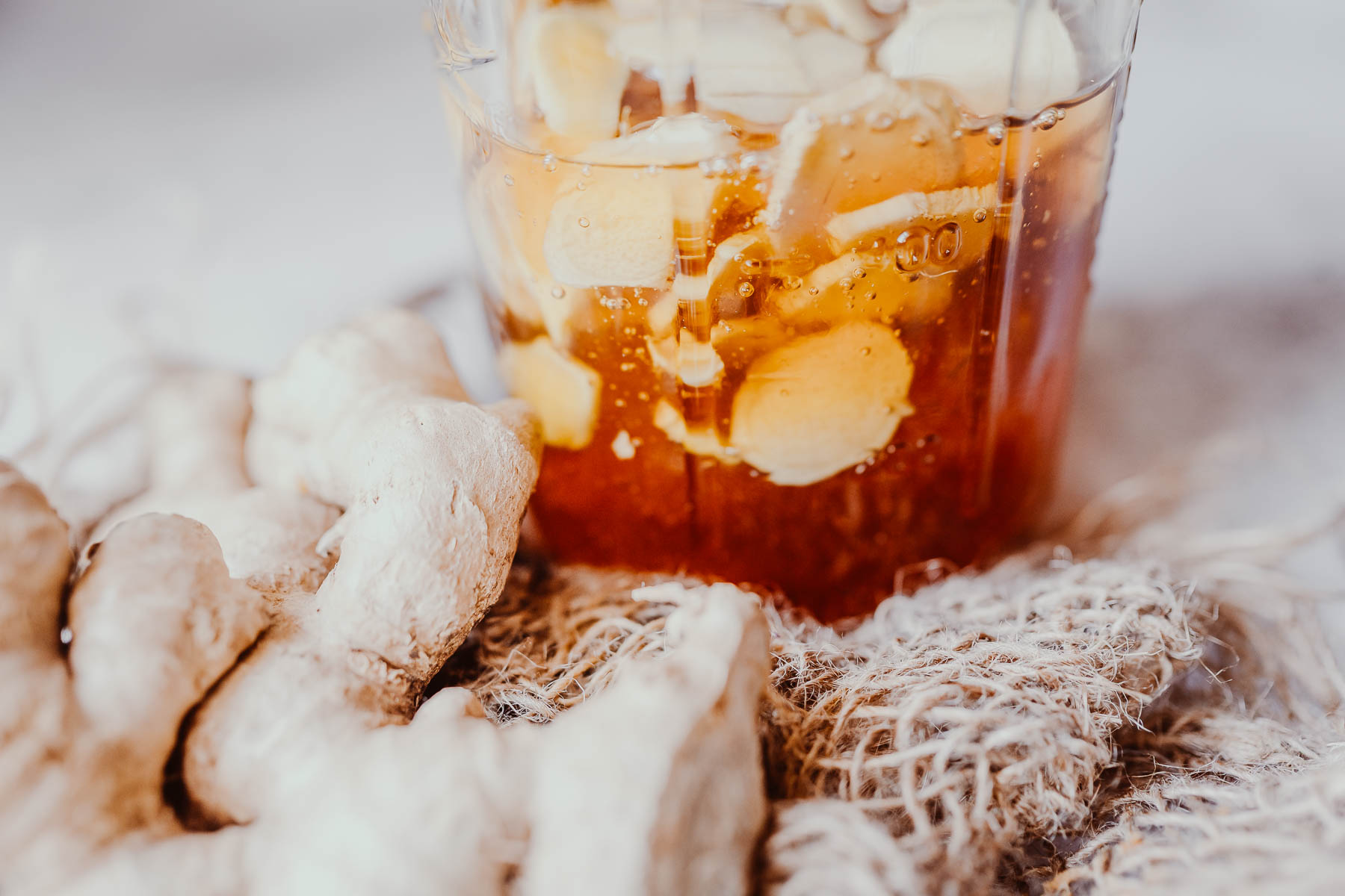 A close-up of ginger roots next to a glass containing ginger slices in honey.