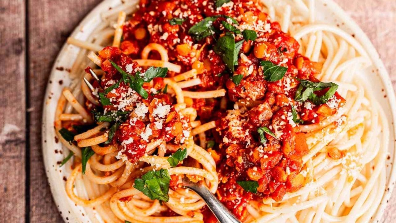A plate of spaghetti topped with tomato-based sauce, lentils, chopped parsley, and grated cheese, with a fork twirling some of the pasta.