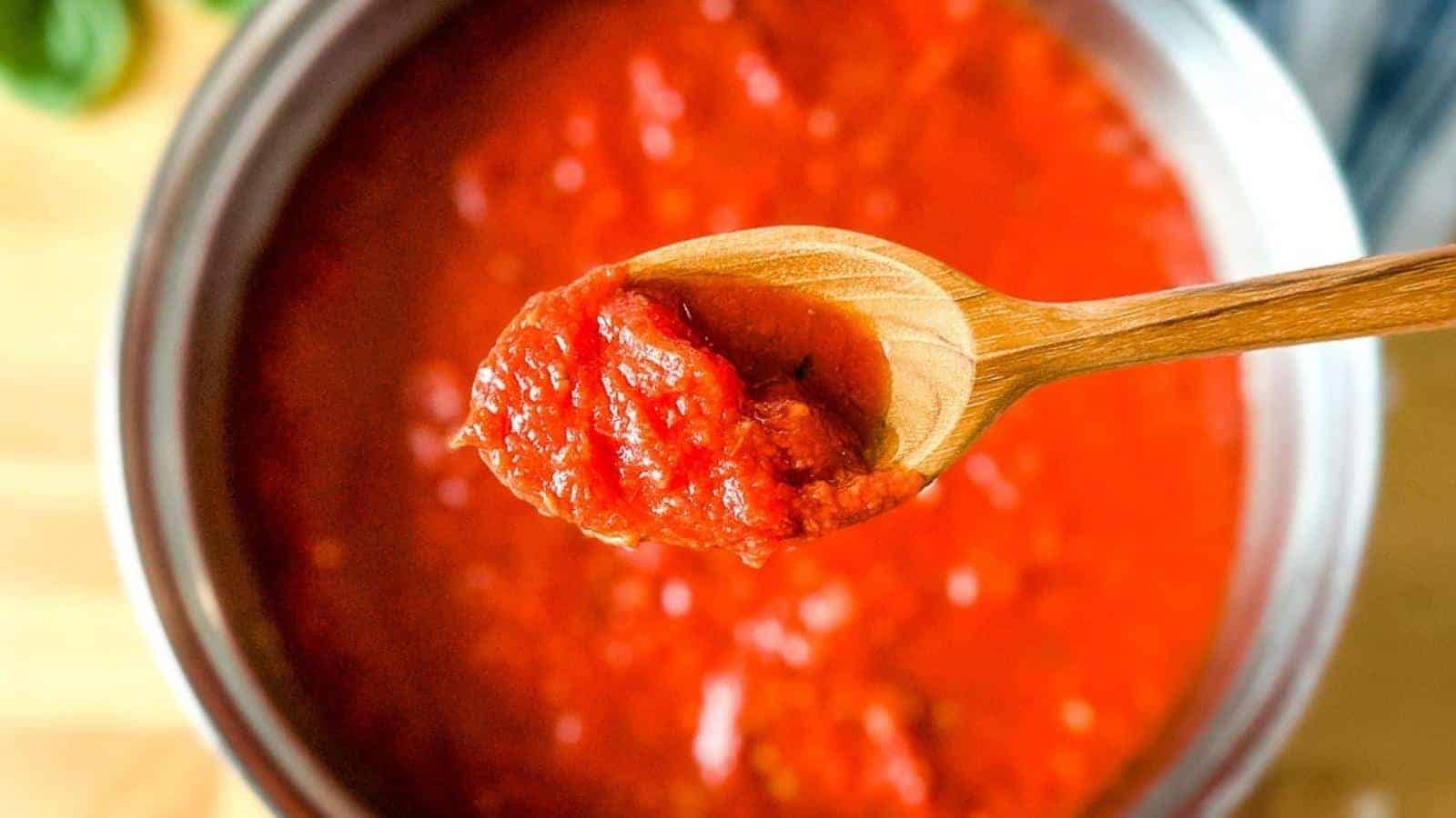 A wooden spoon holds a portion of tomato sauce above a pot filled with more tomato sauce.