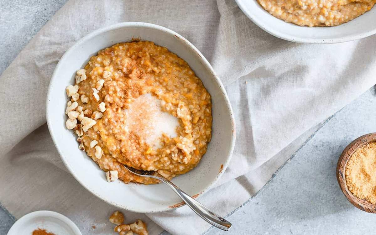 A bowl of oatmeal topped with chopped nuts, cinnamon, and sugar, with a spoon resting in the bowl on a light napkin.