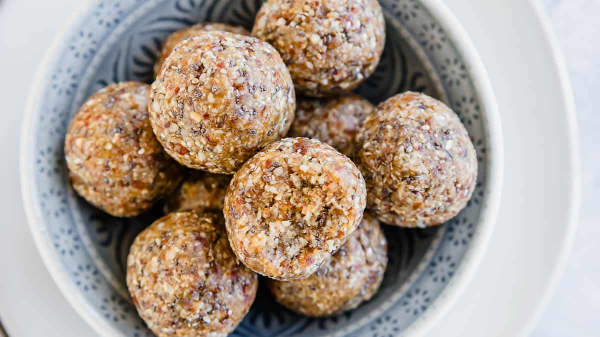 A bowl filled with several round, nut and seed energy balls sits on a patterned plate.