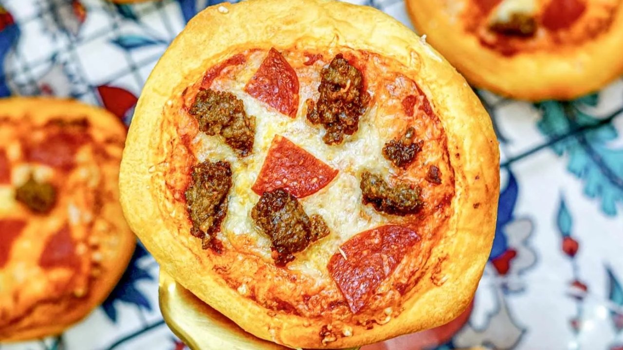 A close-up of a mini pizza topped with melted cheese, pepperoni slices, and sausage on a thick, golden-brown crust.
