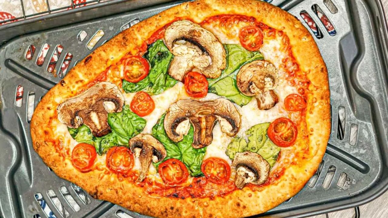 A baked pizza with mushrooms, spinach, and cherry tomato slices on a metal oven tray.