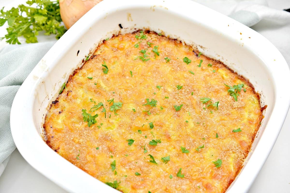 A baked casserole topped with melted cheese and garnished with chopped parsley, in a white square baking dish.