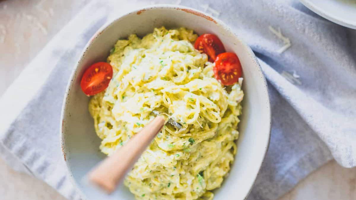 A bowl of creamy spaghetti squash with halved cherry tomatoes on top and a wooden-handled fork placed in the bowl.