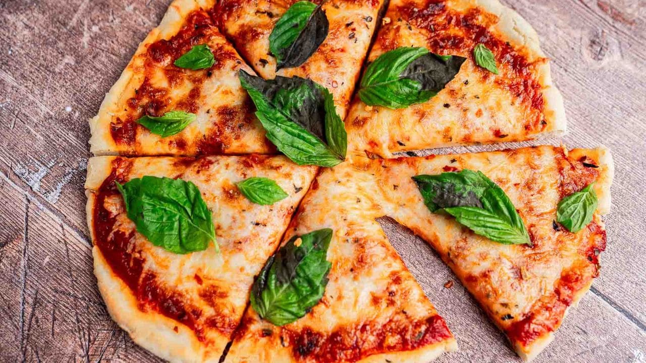 A cheese pizza cut into eight slices, topped with tomato sauce and fresh basil leaves, placed on a wooden surface.