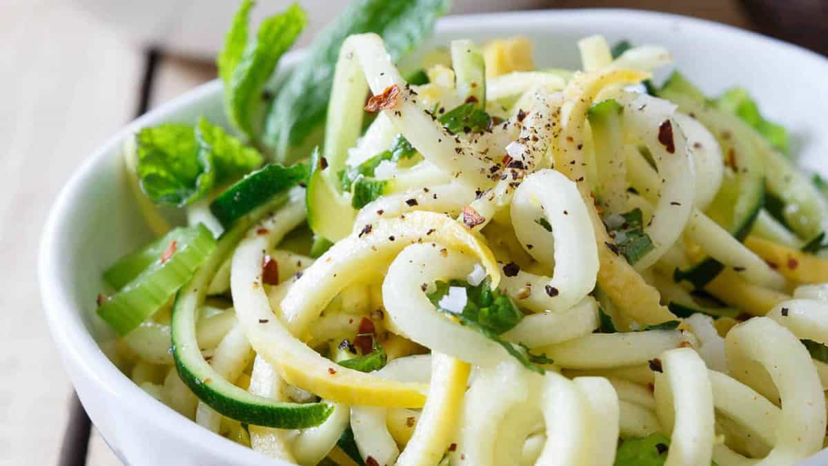 A bowl of spiralized zucchini and yellow squash garnished with herbs and crushed red pepper.