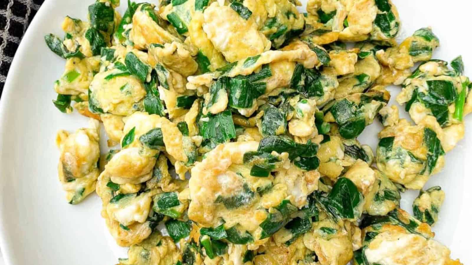Scrambled eggs mixed with chopped green leafy vegetables served on a white plate.