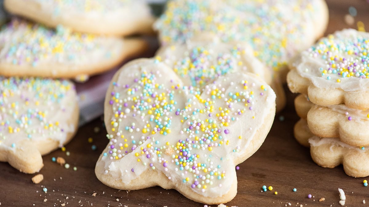 Sugar cookies shaped like butterflies, covered with white frosting and multicolored round sprinkles, displayed on a wooden surface.