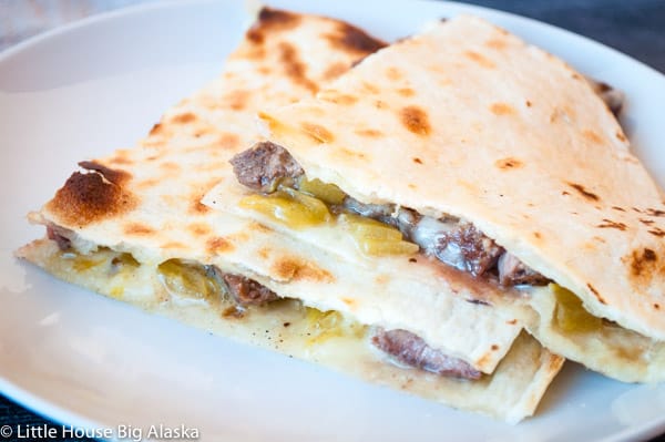 Three triangular quesadilla slices filled with melted cheese, green chilies, and beef, stacked on a white plate.