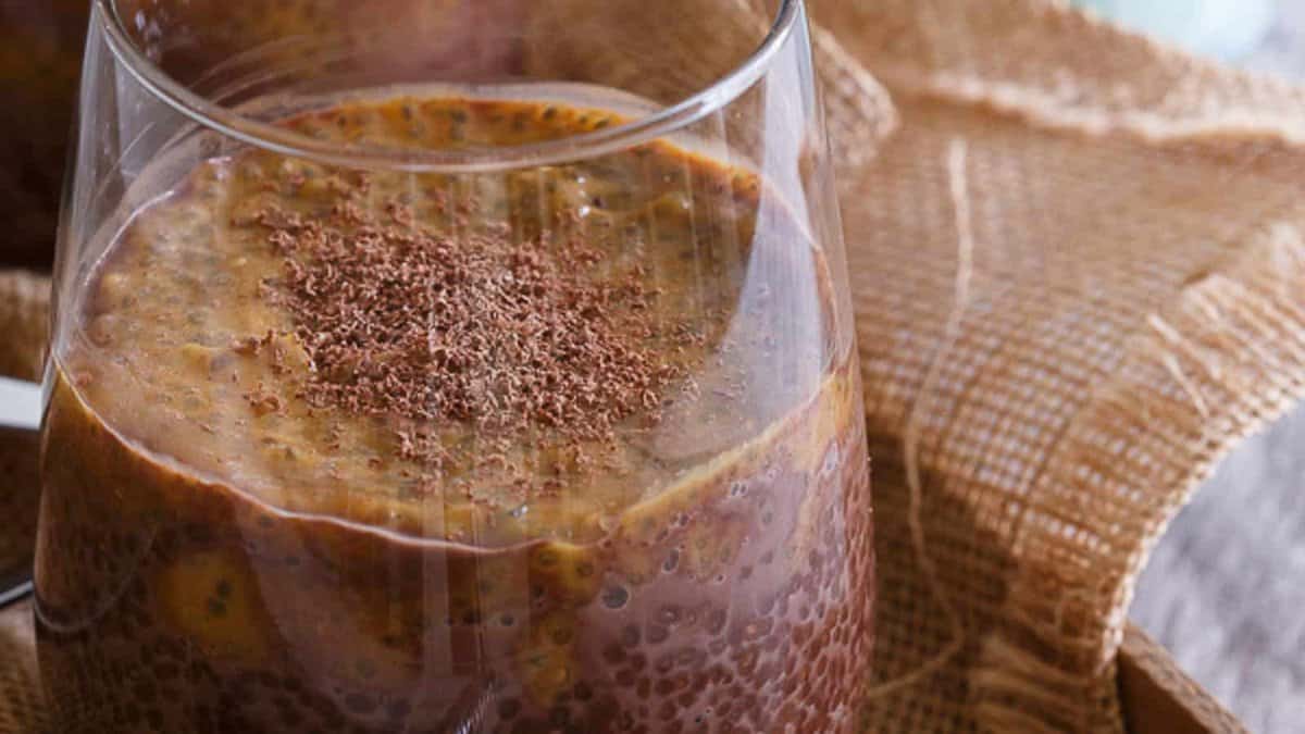 A clear glass filled with chocolate chia pudding topped with grated chocolate, placed on a piece of burlap fabric.