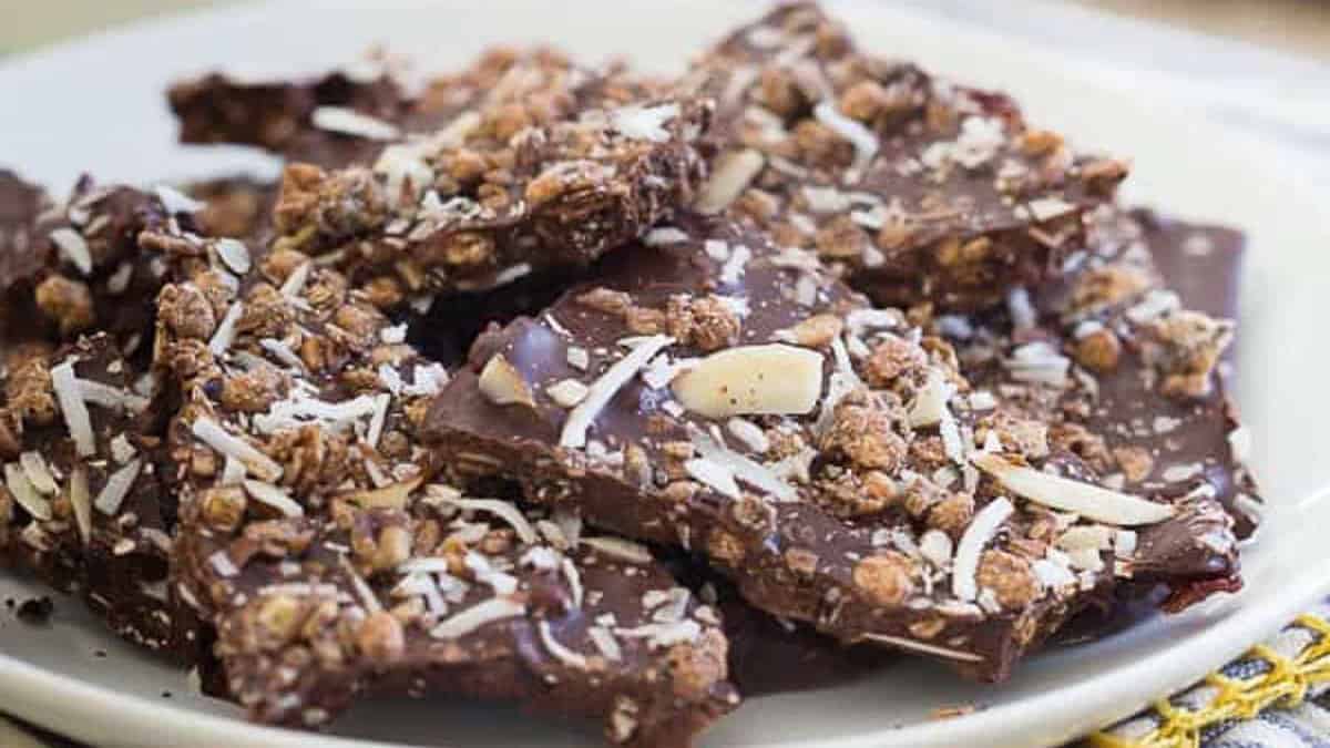 A plate of chocolate bark pieces topped with granola, sliced almonds, and shredded coconut.