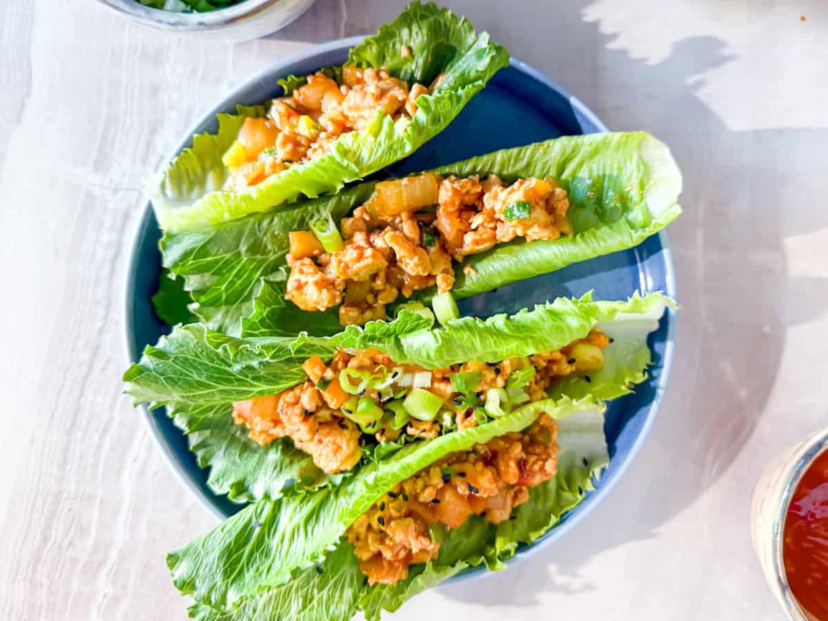 Three lettuce leaves filled with a mixture of diced vegetables and cooked ground meat are arranged on a blue plate.