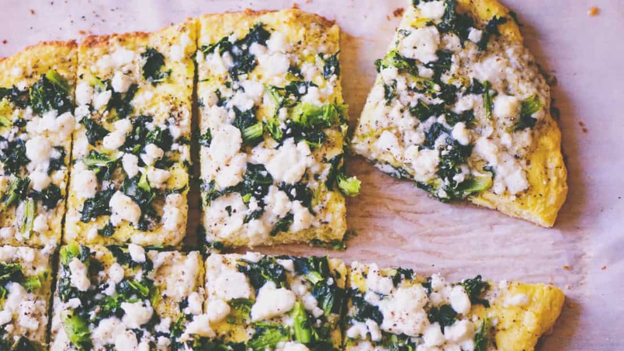 Rectangular slices of flatbread topped with cheese and chopped greens, arranged on parchment paper with one slice slightly separated.