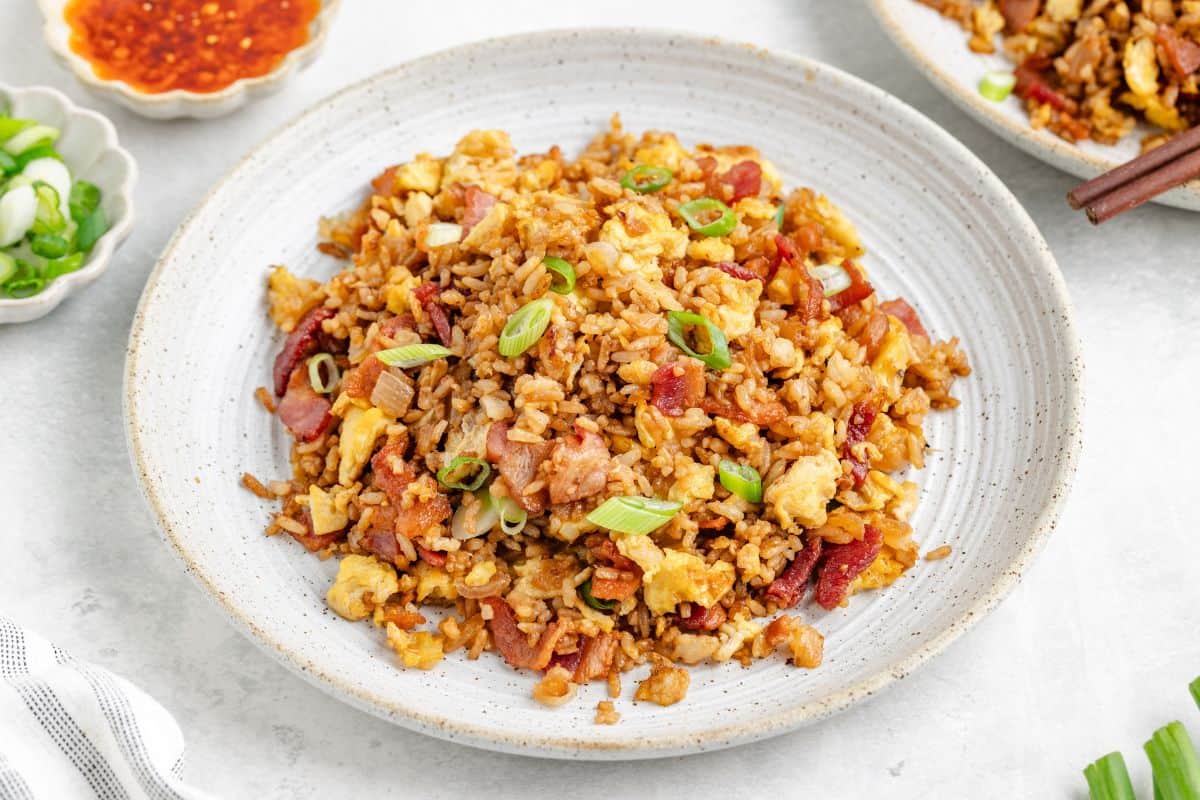 A plate of fried rice with scrambled eggs, sliced green onions, and pieces of meat, served on a white dish.