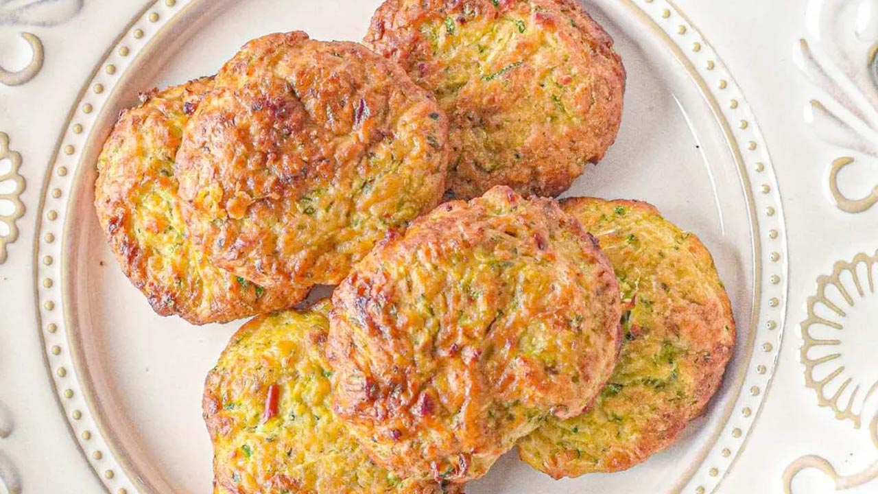 A plate with six golden-brown zucchini fritters arranged in a cluster on a decorative white dish.