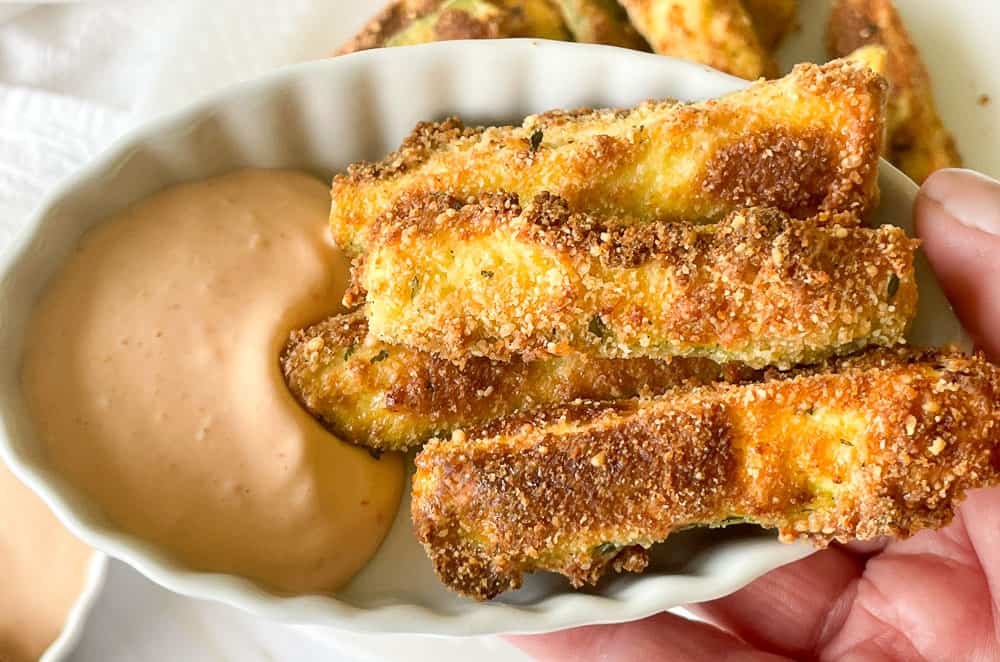 A small dish of breaded and baked zucchini fries served with a side of creamy dipping sauce.